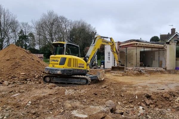 Excavator performing ground excavation for new house construction in a residential area.